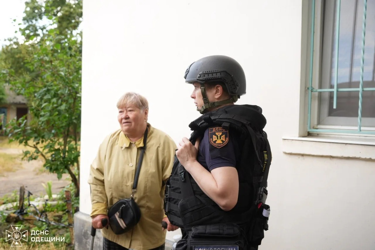 Рятувальник супроводжує літню жінку на милицях від пошкодженого будинку