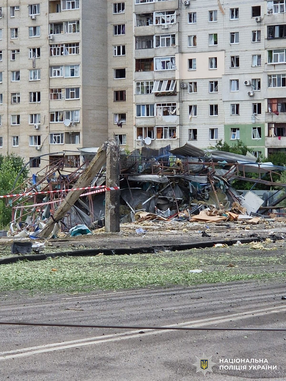Місцева жителька з собакою на руках стоїть неподалік від місця удару в Сумах, на задньому плані видно понівечений транспорт