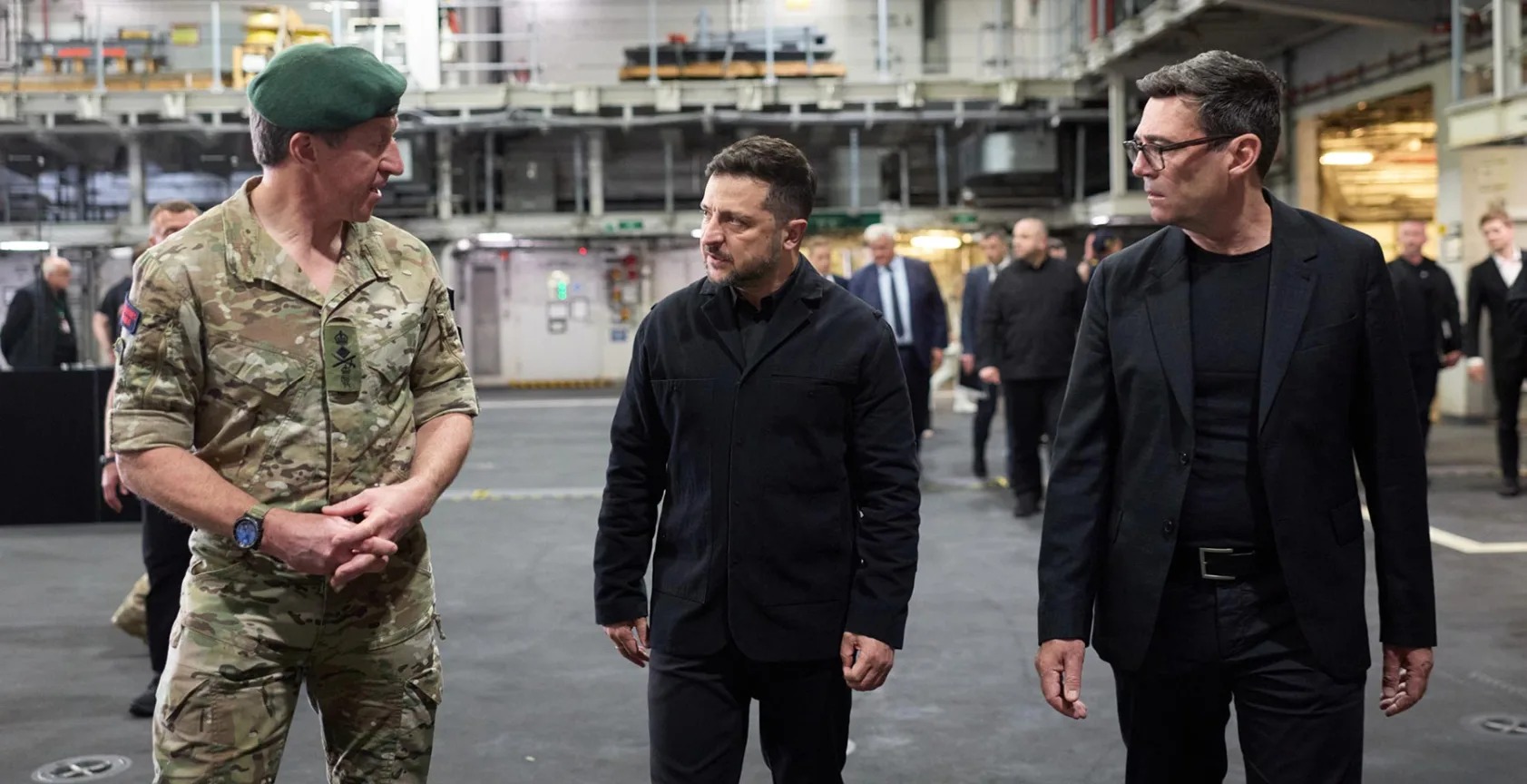 Zelensky and Burnham walk through the aircraft carrier's hangar deck with a Royal Navy officer