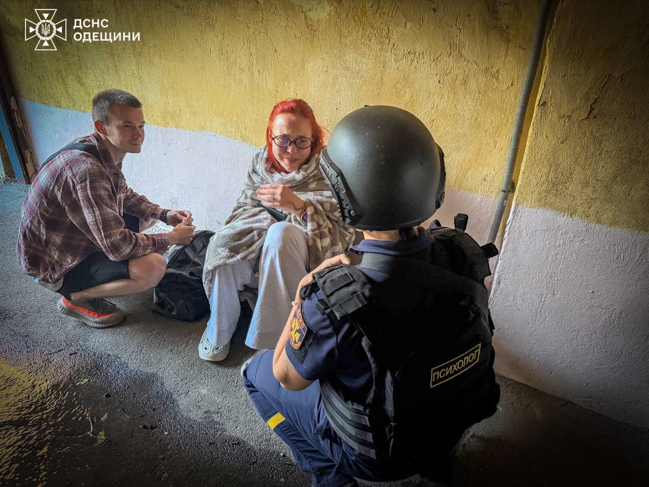 Психолог ДСНС заспокоює постраждалого біля пошкодженого будинку в Одесі