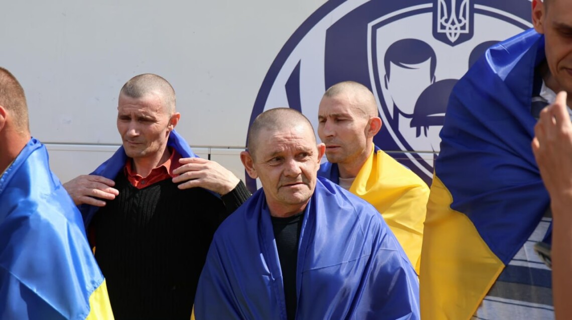 A group of freed defenders wrapped in Ukrainian flags
