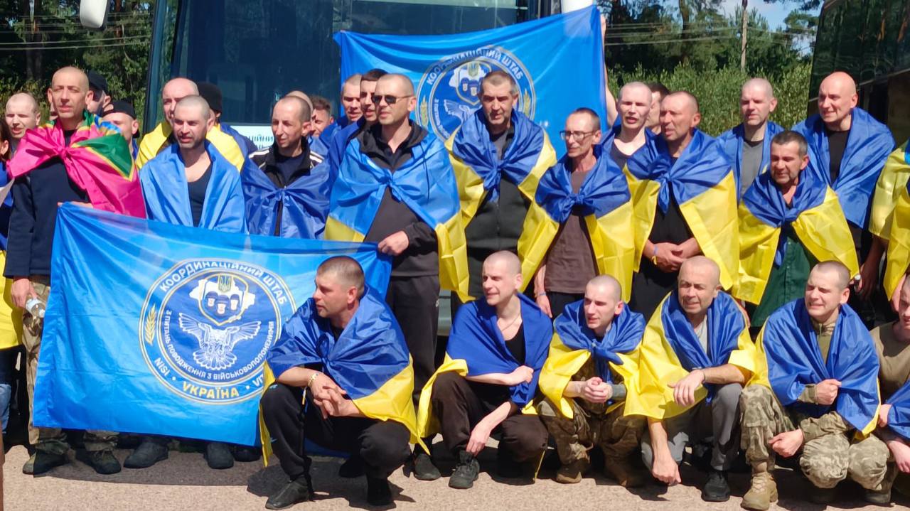 Звільнені українці біля автобуса з прапором Координаційного штабу з питань поводження з військовополоненими
