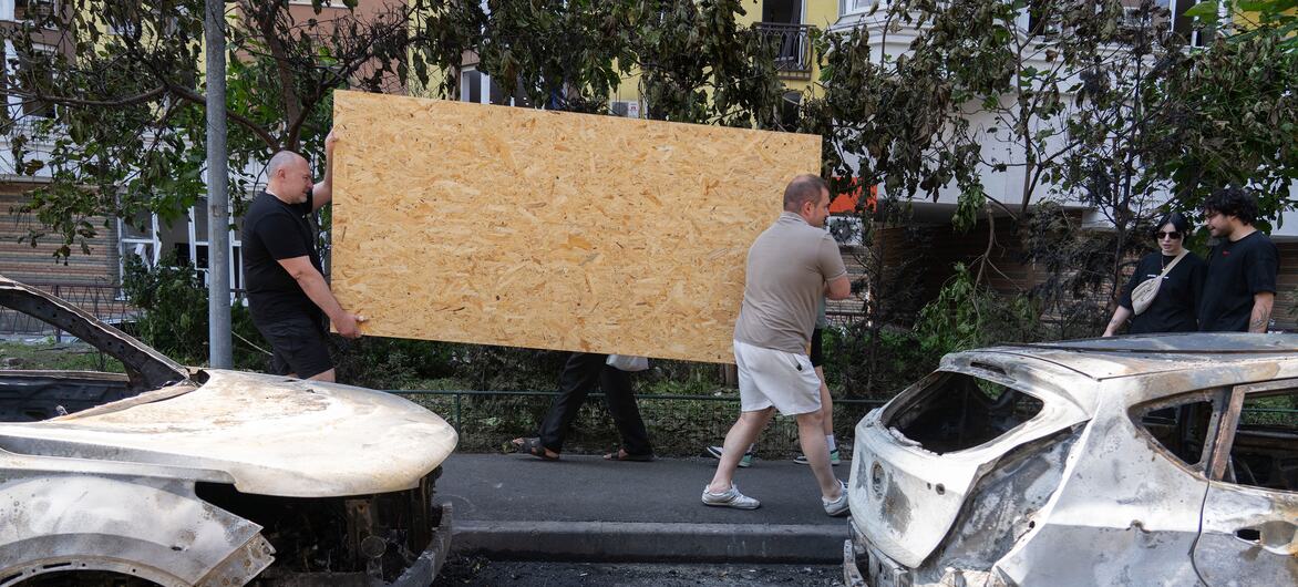 Чоловіки несуть фанеру повз згорілі автомобілі під час відбудови у Києві