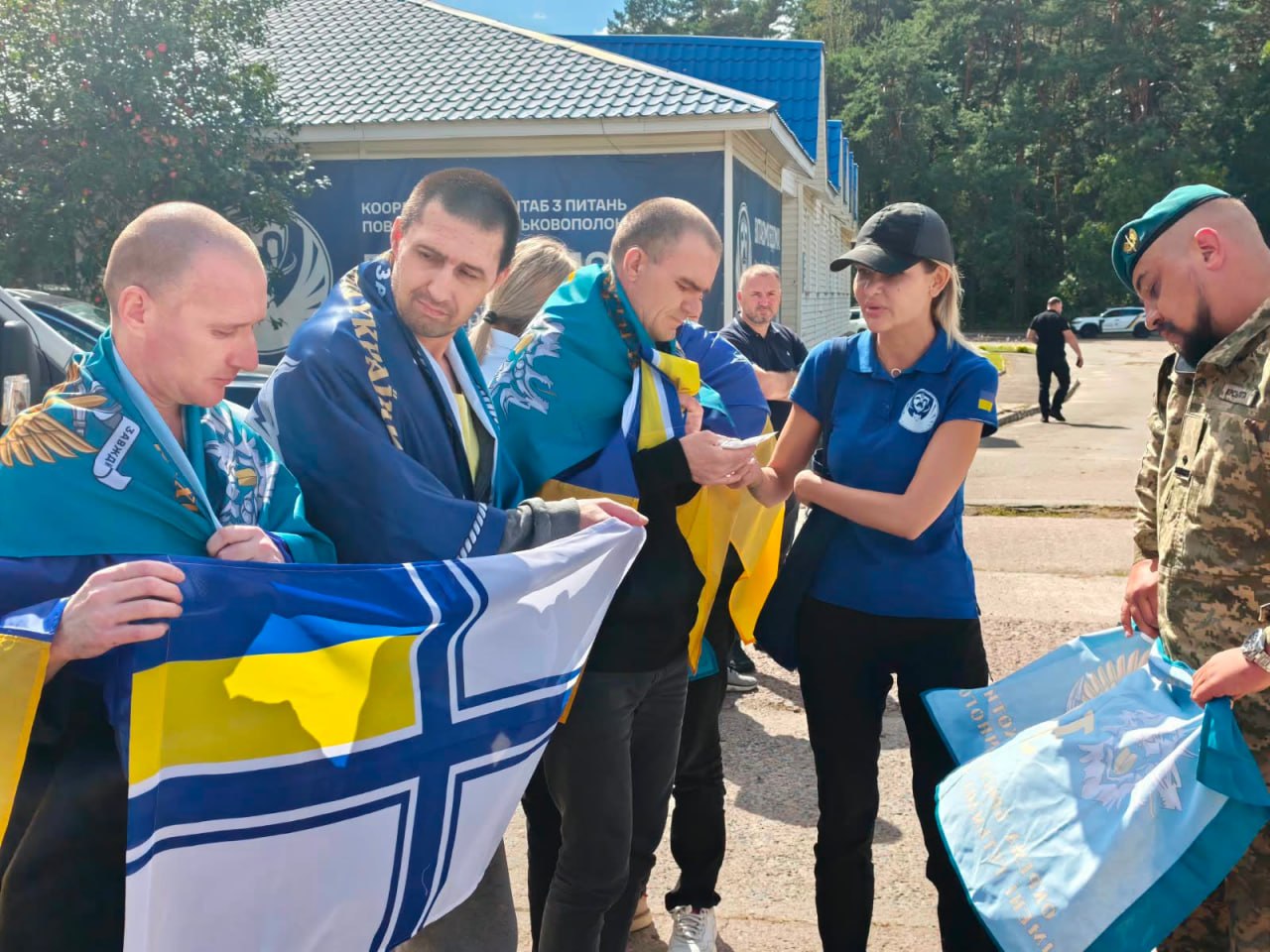 Звільнені військові отримують державні прапори України та символіку від представниці координаційного штабу на пункті обміну