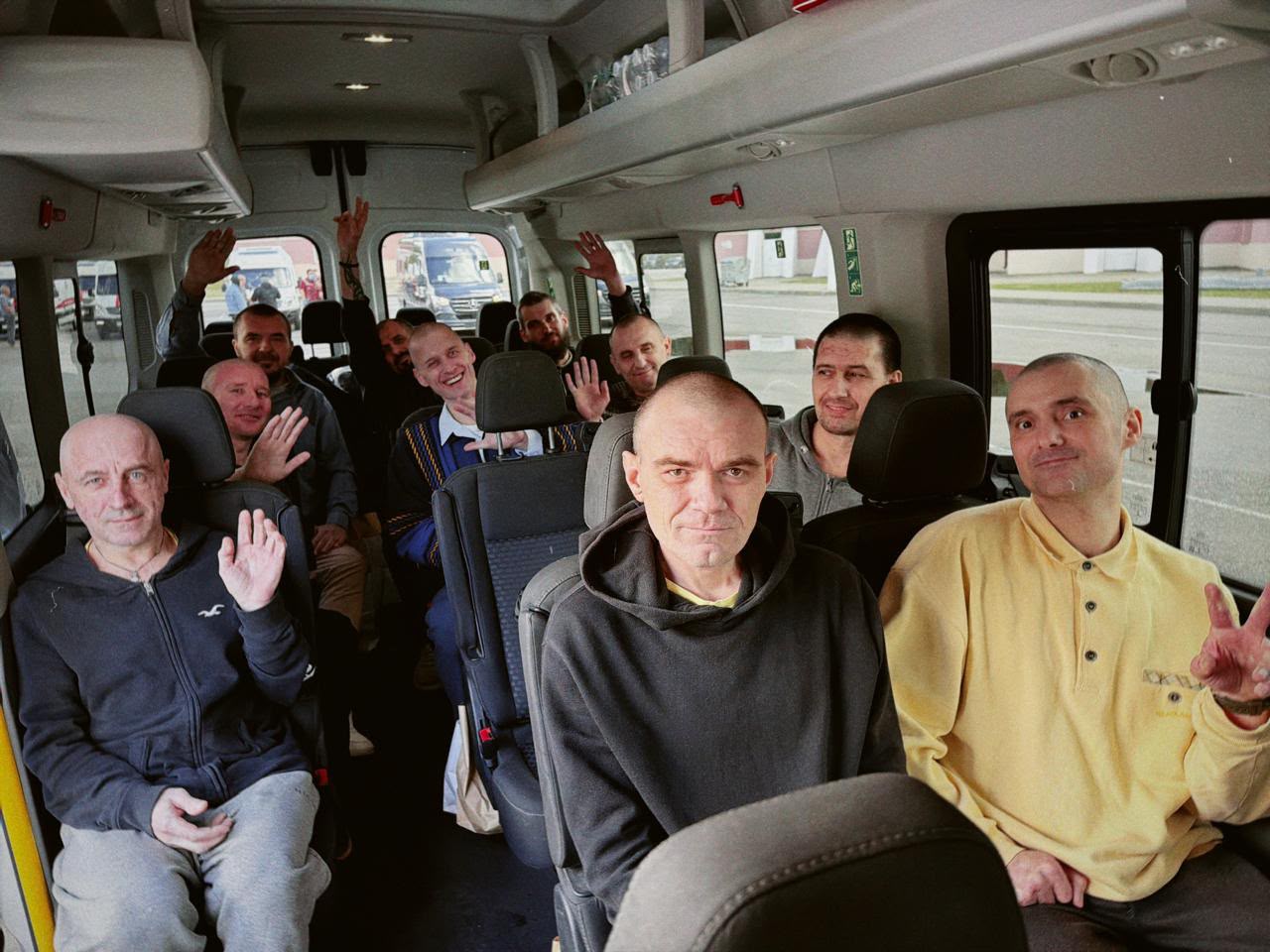 Група звільнених військових у мікроавтобусі усміхається та махає руками дорогою додому