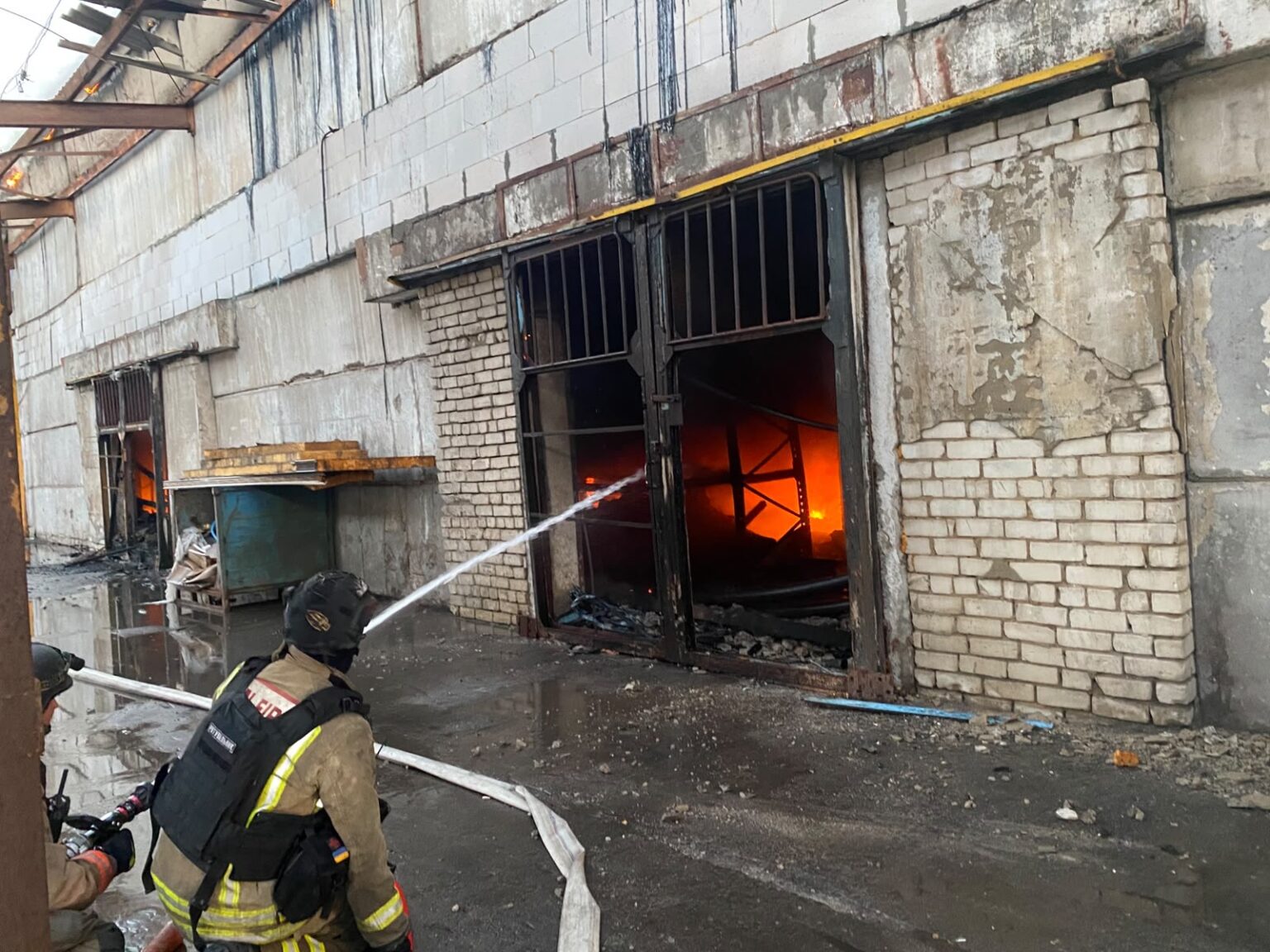 Пожежники гасять активну пожежу всередині складського приміщення, крізь двері видно яскраве полум'я
