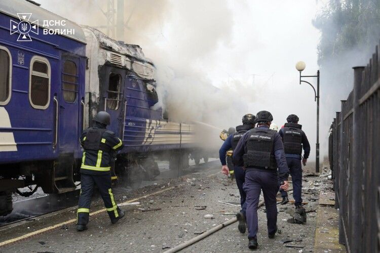 Emergency responders approach a burning passenger train after a drone strike at a Lutsk railway station