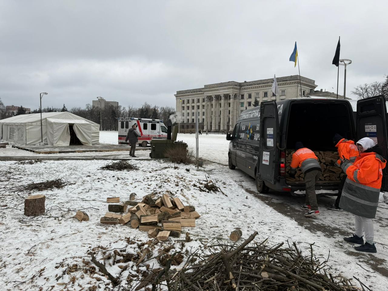 Волонтери завантажують дрова до гуманітарного автомобіля посеред засніженої площі