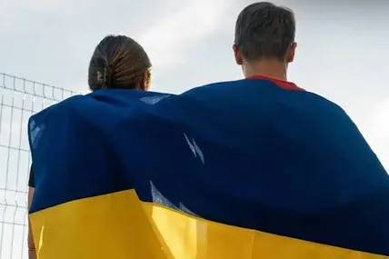 Двоє людей, загорнуті в український прапор, стоять спиною до камери
