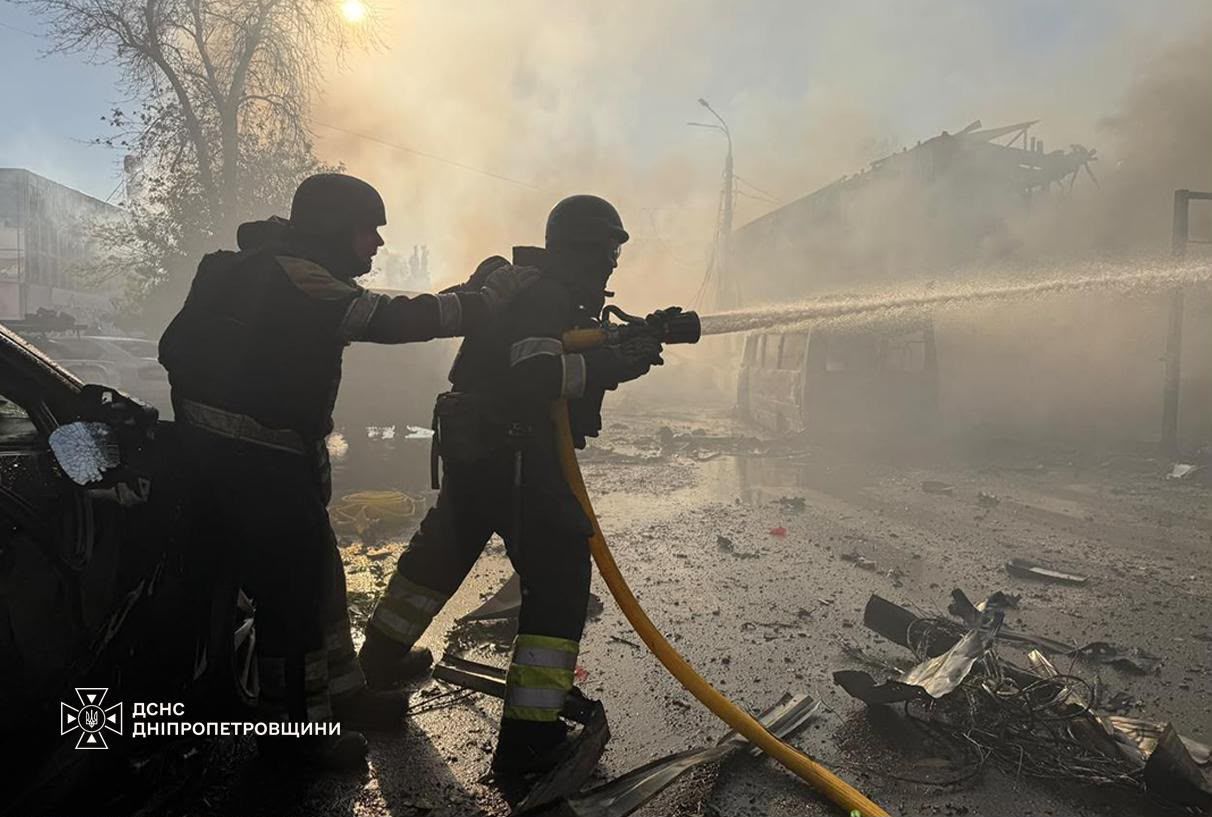 Двоє рятувальників подають воду з брандспойта крізь дим на місці удару в Павлограді