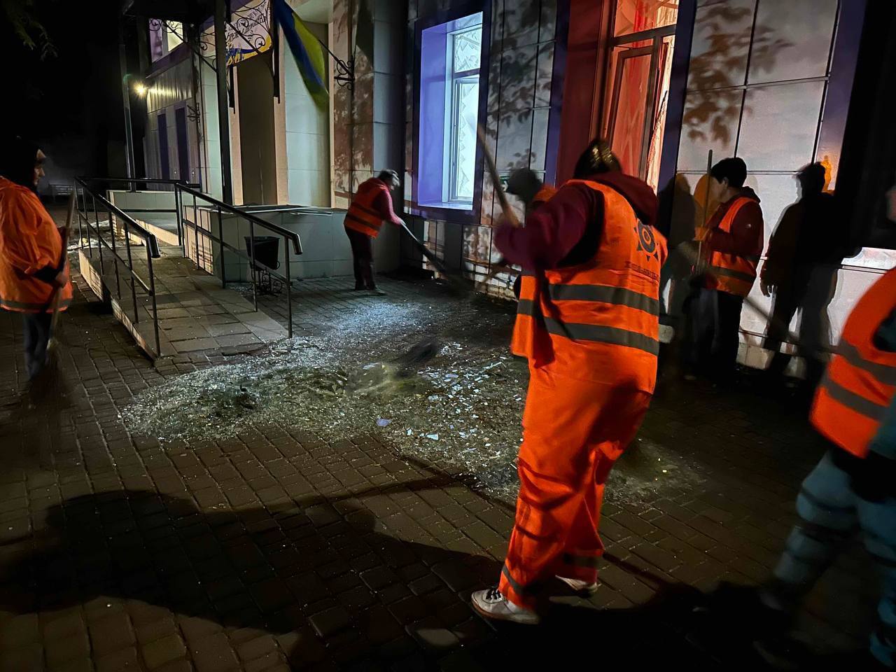 Municipal workers sweep up broken glass outside a damaged building in Odesa region overnight after the strike