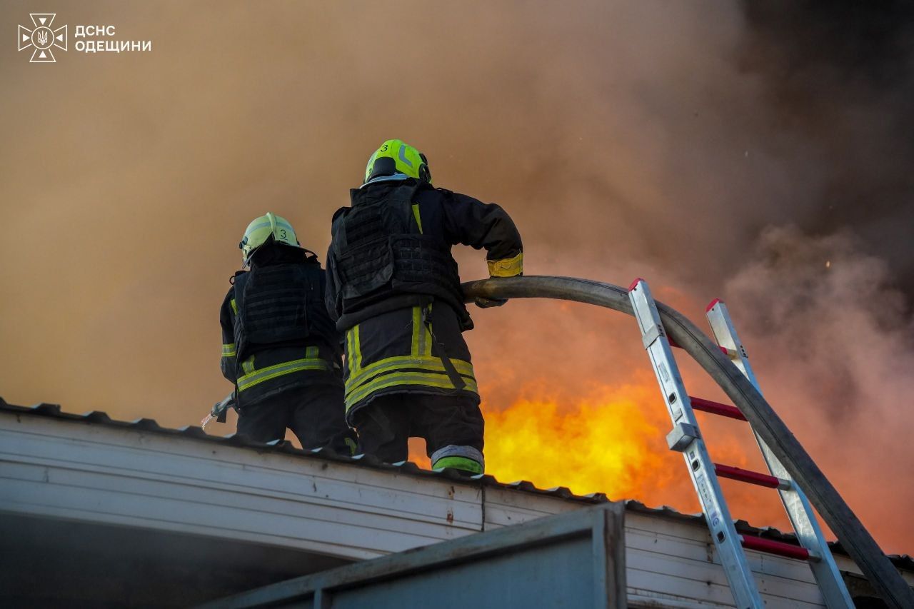 Двоє рятувальників ДСНС Одещини гасять пожежу на даху складу на тлі потужного полум'я