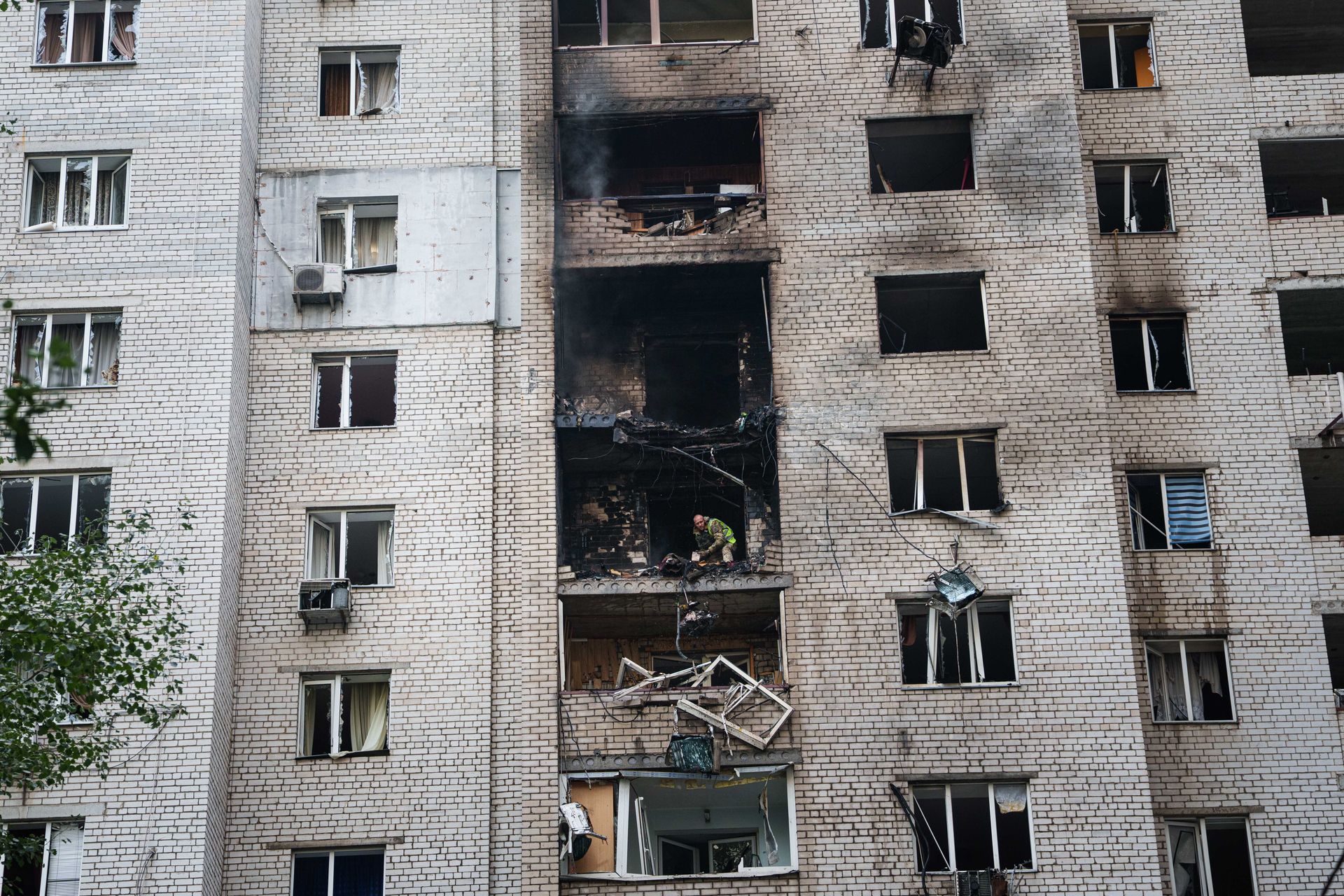 A residential high-rise in Kyiv damaged by a drone strike, with a rescuer clearing debris at the point of impact