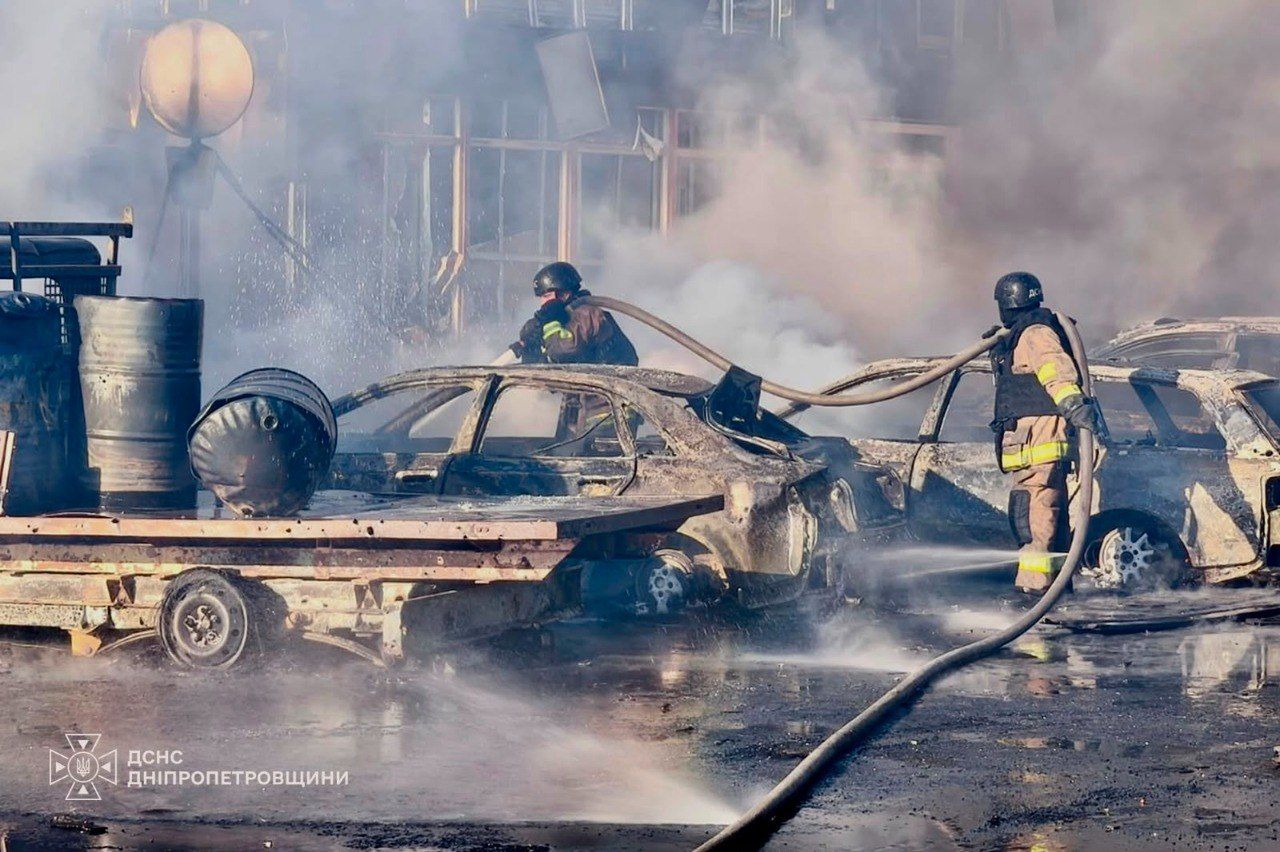Рятувальники гасять рештки вигорілих автомобілів на тлі зруйнованої будівлі в Павлограді