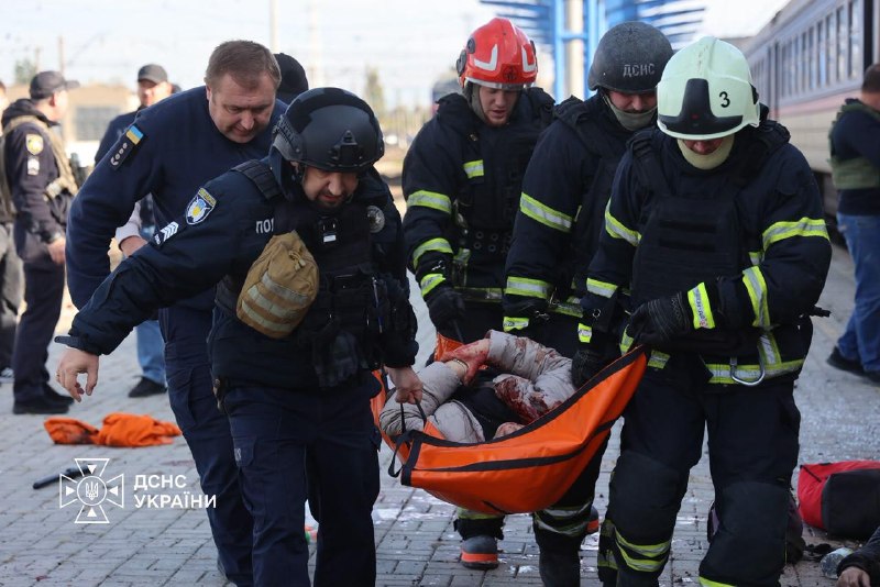 Rescuers and medics carrying an injured person on a stretcher along the platform