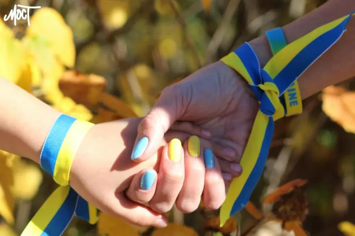 Illustrative image: joined hands with blue-and-yellow ribbons, a symbol of return and support