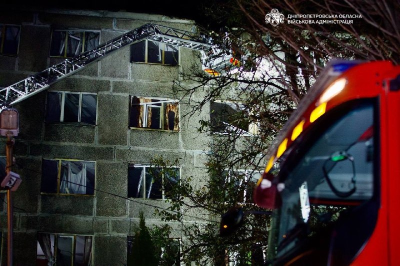 The dormitory building with damaged windows and a rescue vehicle next to it