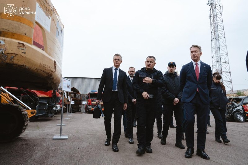 The Norwegian delegation walking with rescuers past burnt-out and damaged vehicles
